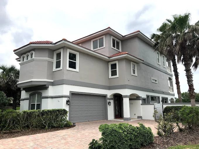Large gray beach house with white bands, windows and garage trim